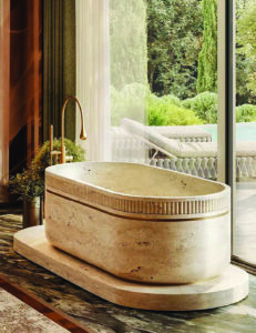 Oval travertine bathtub with a fluted upper band, set on a matching stone plinth