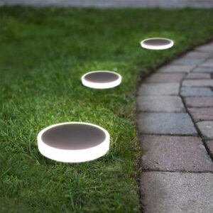 Flat circular in-ground garden lights set along a lawn edge beside a paved path