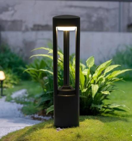 Black post bollard with a wide circular disc head lighting a planted garden path at night